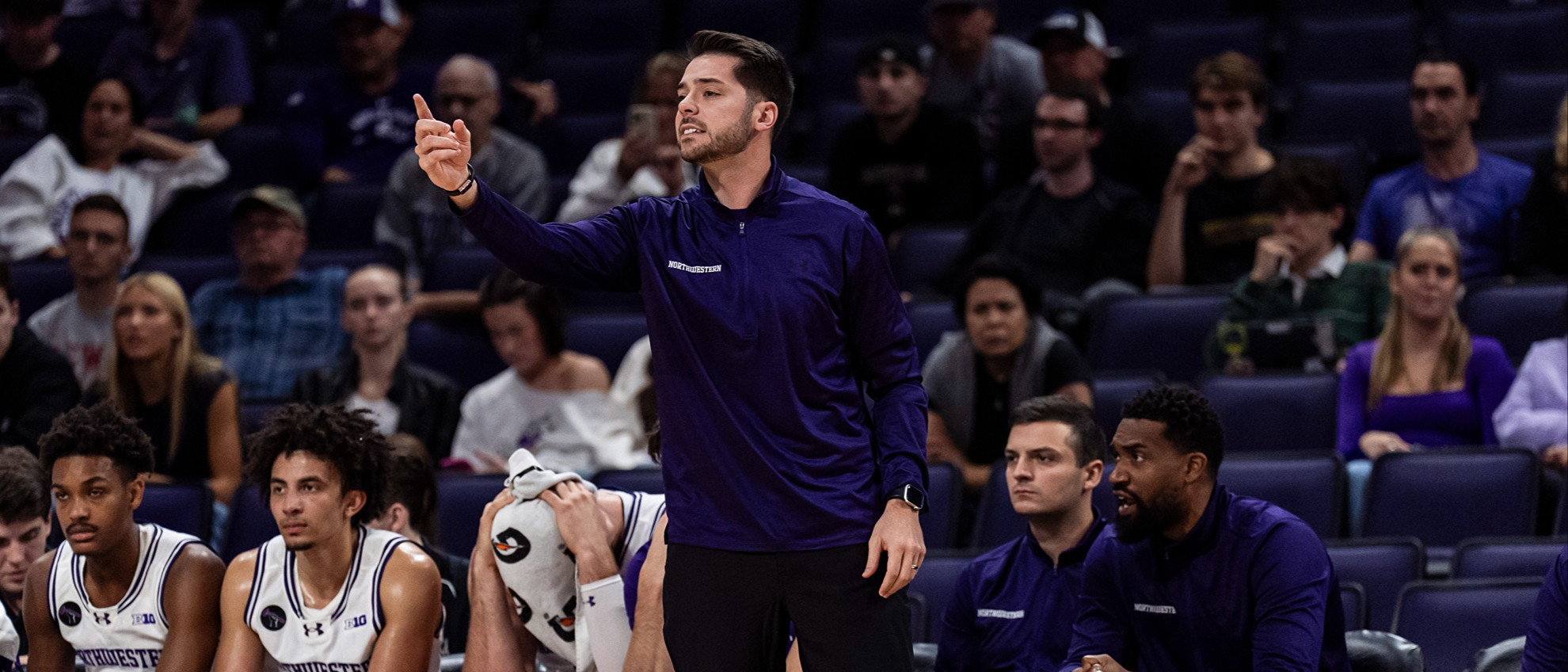 20241030_MBB_LEW_RK_092.jpg Northwestern assistant coach Bryant McIntosh points toward the floor while standing up on the bench.